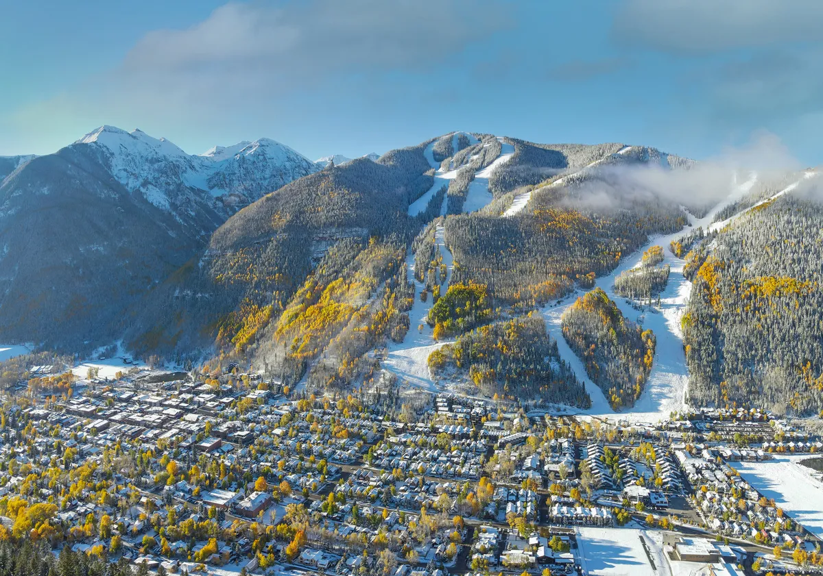 A panoramic view of snow-covered mountains, ski slopes, and a bustling town below. The scene exudes both the thrill of outdoor activities and the welcoming atmosphere of a mountain community.