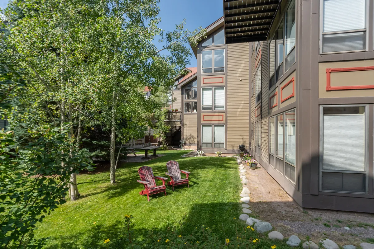 This image features a lush, green lawn with red Adirondack chairs set out, surrounded by trees and the architectural elements of the building in the background. The space is clearly meant for relaxing, socializing, and enjoying the outdoors, making it perfect for families or groups. The well-maintained grass and seating evoke a welcoming community vibe.