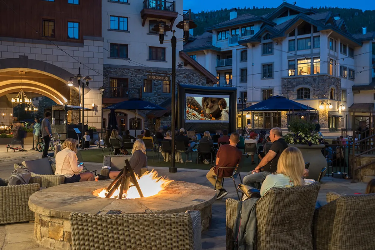 An inviting outdoor space featuring a fire pit surrounded by comfortable seating and an outdoor movie screen, set up for a communal experience. The area is ideal for group gatherings, watching movies under the stars, or spending quality family time together in a safe, relaxed environment.